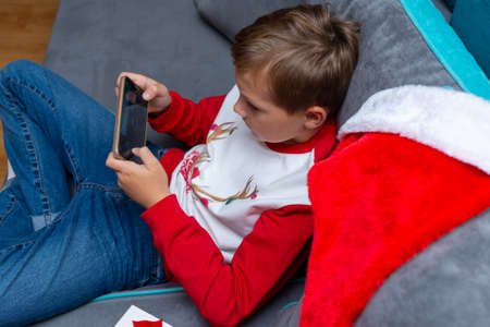 Top view Attractive kid boy using smartphone on Christmas holidays white gift for xmas photo at home