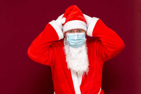 Closeup Santa Claus keep his head medical mask making a stop gesture with his hands on red backgroundの写真素材
