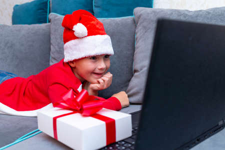 Happy kid boy meets Christmas through a video call with friends during pandemic coronavirus.Close up side view.の写真素材