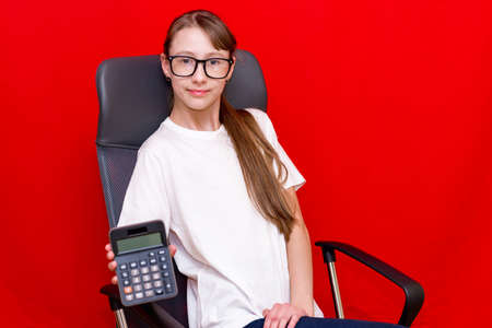 Young surprised caucasian girl counting calculator. Education concept.Red studio background.の写真素材