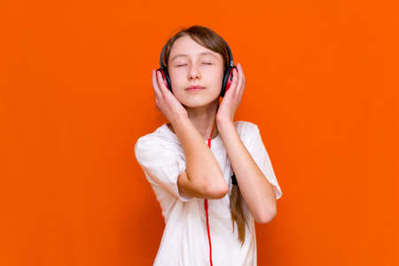 Attractive 12s girl in white t-shirt listens to music on red headphones closeup in a studio indoorの写真素材