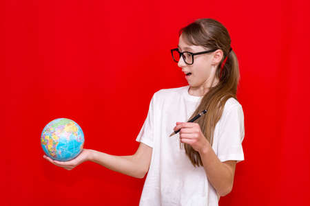 Close up surprised teenager girl holding earth globe eyewear pen on red studio backgroundの写真素材