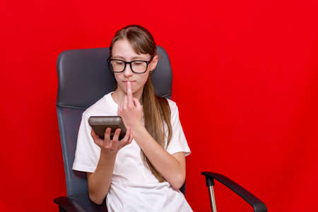 Young surprised caucasian girl counting calculator. Education concept.Red studio background.の写真素材