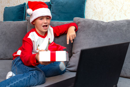 Amazed child shows present Christmas through a video call with friends during pandemic coronavirus.boy is using a laptop.の写真素材