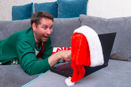 Male man virtually exchanging Christmas gifts and having video call over a laptop at home on the couch.の写真素材