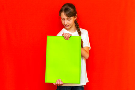 Front view teenager girl showing blank paper.Mock up,banner,copy space.Bright red studio background.の写真素材