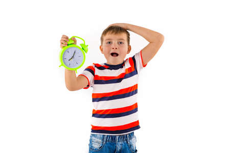 shocked cute boy holding alarm clock on white isolated studio background.の写真素材