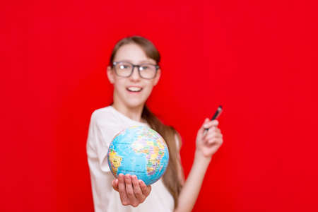 Close up teenager girl holding earth globe eyewear pen on red studio backgroundの写真素材