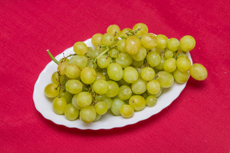 Green grape on a white plate. Red background. Top view.の写真素材