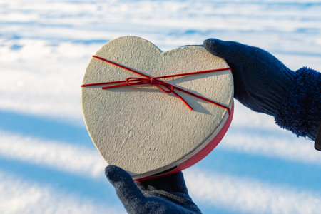 Woman hands holds a heart shape gift in her hands winter outdoors park. Valentine's day concept.の写真素材