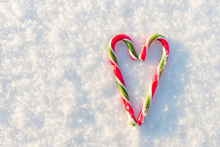 Two flat lay candy canes forming a heart shape on the snow.Top view.の写真素材