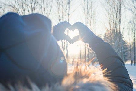 Woman making heart symbol with hands wearing gloves, sunny winter evening, sunrays, Valentines day, Love concept.の写真素材