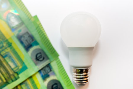 One LED bulb and 100 euro bills on white light backgroundの写真素材