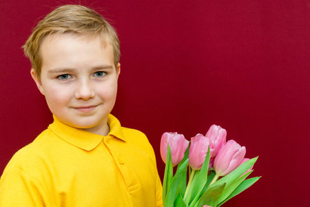 Caucasian boy holding a bouquet of tulips and looks at the camera. Mother's Day, March 8,...