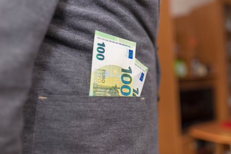 One hundred euros and a man's jacket pocket indoors shot.Blurred background.の写真素材