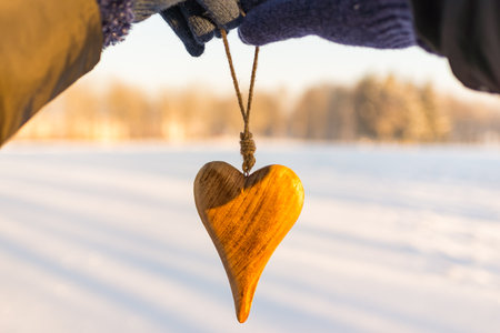 Two couple hands and a wooden heart on a sunset background.Forest winter blurry background.の写真素材