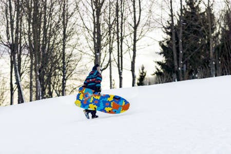 Small boy with snowboard on the nature.He go up a mountain at evening.