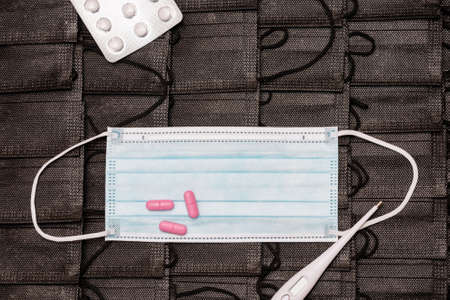 Protective medicine mask,thermometer and pills on pile black face masks background. flat lay top view.の写真素材