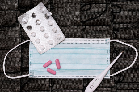 Protective medicine mask,thermometer and pills on pile black face masks background. flat lay top view.の写真素材