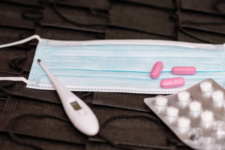 Protective medicine mask,thermometer and pills on pile black face masks background. flat lay top...