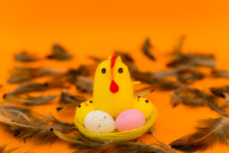 Yellow chick seat on a nest with colored plastic Easter eggs on blurred yellow backgroundの写真素材