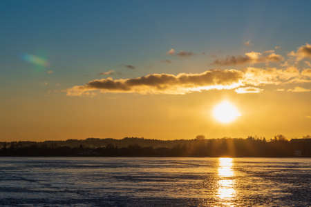 Winter landscape with frozen lake at sunrise or sunset. Lake glistening ice reflects the sun.Forest...