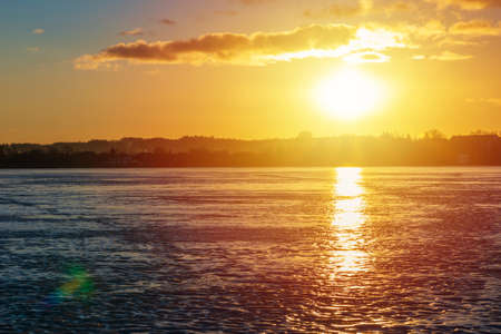 Winter landscape with frozen lake at sunrise or sunset. Lake glistening ice reflects the sun.Forest...