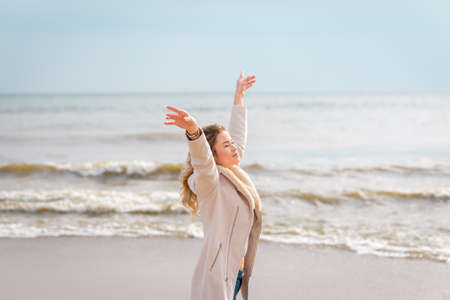 Relaxed woman, arms rised, enjoying spring sun, on a beautiful beach. Young lady feeling free,...