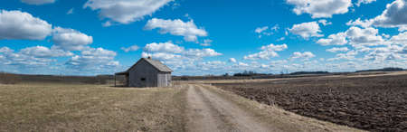 An old abandoned small wooden house in the fields sky clouds, next to a path barn or scary concept.Panoramic view.の写真素材