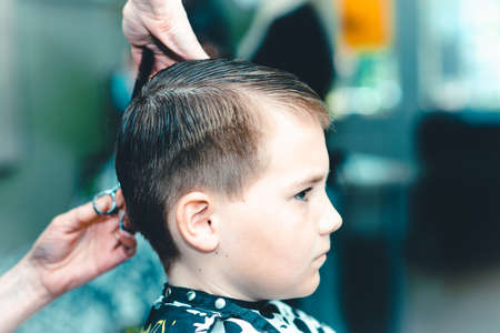 One Cute little boy getting haircut by hairdresser at the barbershop.Side view.Closeup.Toned.の写真素材