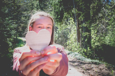 One joyful teen girl in forest holding a wooden heart in her hands.On spring or summer nice sunny day.Selective focus.の写真素材