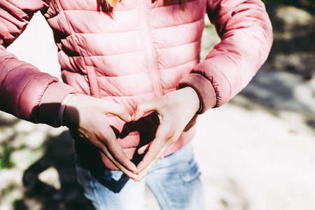 Hands in heart shape. Teenage girl hands heart shape on against forest path background of summer or...
