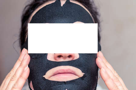 Young woman apply black cosmetic fabric facial mask at home. Face peeling mask,spa beauty treatment,...