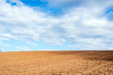 Plowed brown field and white clouds on blue sky.cloudy sky over brown field.Nice Spring summer day.の写真素材