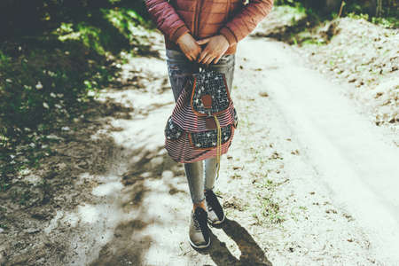 One teen girl in a casual clothes holds backpack on the sandy road in forest of spring or summer trees.Sunny summer day.Cropped image.Toned.の写真素材