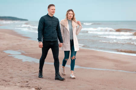 Attractive young couple walking along the shore of a sandy beach, on a spring romantic holiday, outdoors. Travel tourists lifestyle. Couple enjoying loving time together.の写真素材