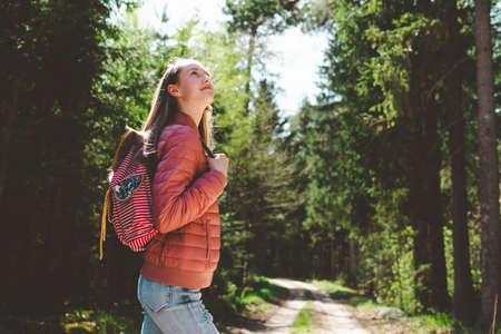 Pretty one teen young tourist girl relaxing on forests road.Teenage with backpack on green forest summer or spring.Closeup.の写真素材