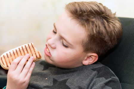 A Hungry boy eating a hot dog at home kid eats a hot-dog sandwich.Indoors shot.Closeup.の写真素材