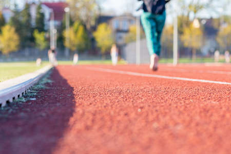 A woman running on the treadmill of a stadium around a football field. Artificial cover of the sports complex. Activity for weight loss and a healthy lifestyle.Selective focus.の写真素材