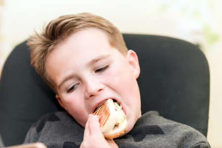A Hungry boy eating a hot dog at home kid eats a hot-dog sandwich.Indoors shot.Closeup.の写真素材