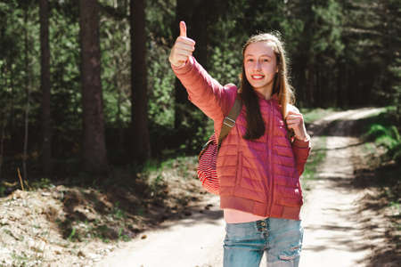 One cheerful brown-haired traveler teen girl, showing thumb up.Close up of teenager hand gesturing thumbs up in a park Spending spare time in wild wood.Summer sunny day.の写真素材