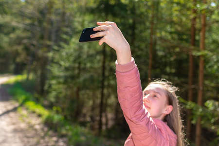 Young teen girl traveler taking selfie on mobile phone in a summer day forest. Smiling girl looking...