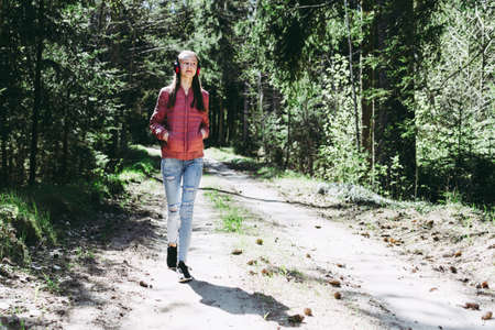 One lovely cheerful slim fit thin teen girl enjoying, listening to music in the forest while walking summer,spring day forest or park.Front view.の写真素材