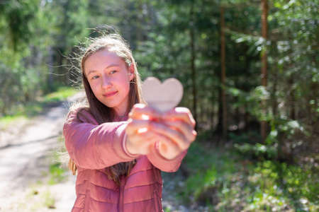 One joyful teen girl in forest holding a wooden heart in her hands.Girl showing wooden heart.On spring or summer nice sunny day.Selective focus.の写真素材