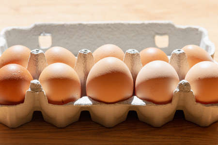 Fresh chicken eggs background. Brown eggs in craft carton pack on hay at rustic wood table.Top view....