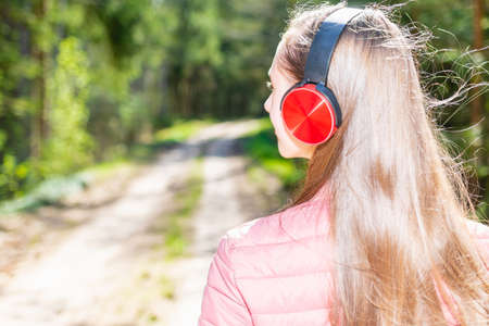 One lovely cheerful slim fit thin teen girl enjoying, listening to music in the forest while walking summer,spring day forest or park.Back view,closeup.の写真素材
