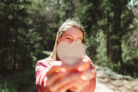 One joyful teen girl in forest holding a wooden heart in her hands.On spring or summer nice sunny day.Selective focus.の写真素材