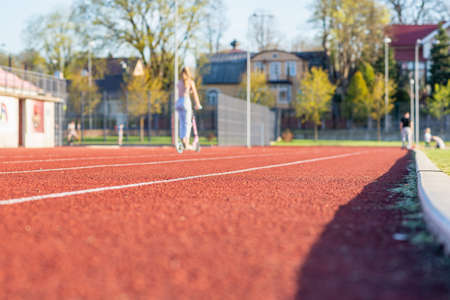 One woman with scooter on the treadmill of a stadium around a football field. Artificial cover of the sports complex. Activity for weight loss and a healthy lifestyle.Selective focus.の写真素材