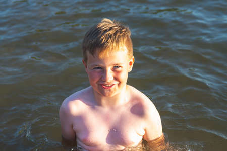 Cute young boy enjoy having fun at lake or beach water on warm sunset evening time outdoors.Happy childhood vacation at countryside concepton.Boy at pier warm summer day having good time in a water.の写真素材