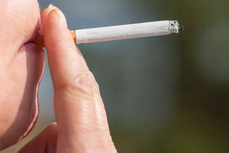 Middle age woman smoking cigarette outdoors with sun on her face. Close up of a girl with a...